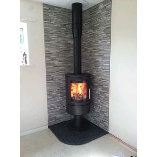 Contemporary woodburner on a pedestal on a honed granite corner hearth and tiled walls behind
